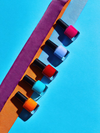 A selection of colorful nail polish bottles are arranged on a blue surface with several bright colored ribbons.の素材