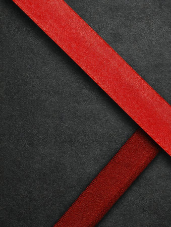 Two red ribbons cross each other on a dark gray surface, creating a simple abstract geometric pattern.の素材