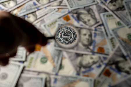 A hand holds a magnifying glass focused on a US dollar bill surrounded by more bills on a flat surface.の写真素材