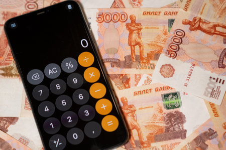 A smartphone displays a calculator app while resting on various denominations of Russian currency, ideal for budgeting.の写真素材