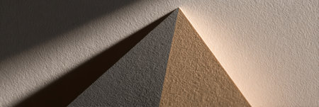 A paper pyramid with different shades rests on a surface, illuminated by soft light, creating unique shadow patterns.の素材