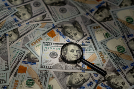 A magnifying glass zooms in on details of many hundred dollar bills in a financial context.の写真素材
