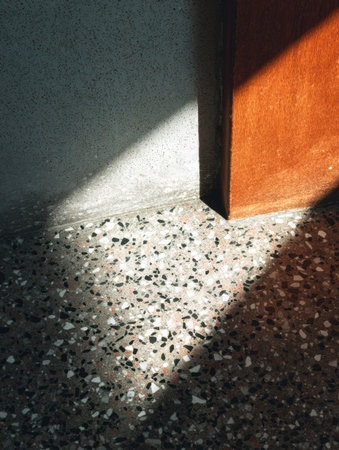 Soft sunlight illuminates a speckled floor while contrasting shadows create an inviting atmosphere beside a door.の素材