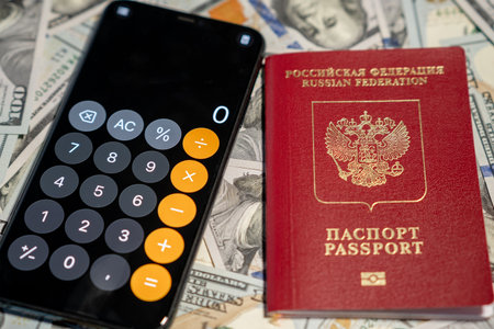 A calculator displays numbers beside a Russian passport and piles of cash, suggesting financial planning or travel.の写真素材