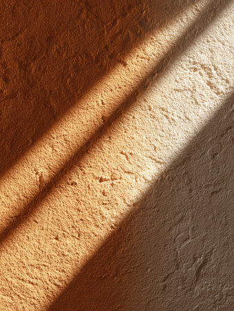 Soft light casts lovely shadows on a textured wall, revealing warm tones and intricate details at golden hour.の素材
