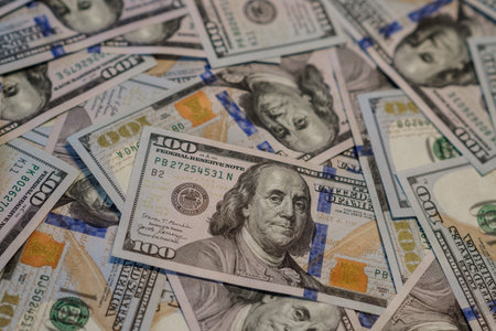 Scattered hundred dollar bills on a flat surface showcase intricate designs, evoking wealth and...
