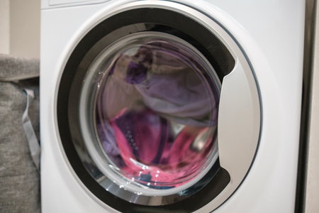 A front-loading washing machine is in action, cleaning colorful clothes during daytime hours at a...