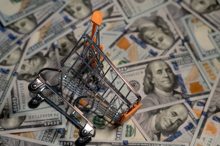 A small cart rests on a spread of hundred-dollar bills, highlighting shopping and money management...