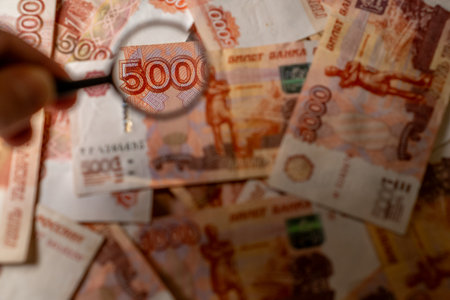 A person examines a 500 banknote using a magnifying glass, with various bills spread across the table.の写真素材