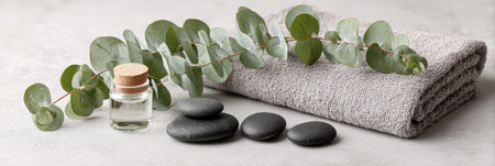 A peaceful spa arrangement features eucalyptus leaves, smooth stones, and a bottle of essential oil on a soft towel for relaxation.の素材