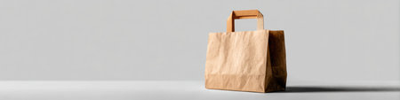 A brown paper bag rests on a simple white surface, casting a soft shadow in a calm environment with gray hues.の素材