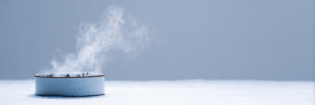 Delicate tendrils of incense smoke curl into the air from a blue holder placed on a smooth surface, creating a serene atmosphere.の素材