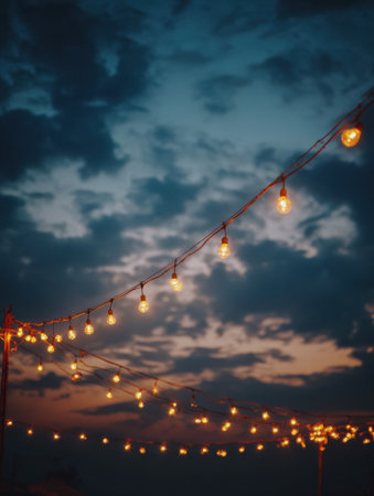 String lights glow softly against a vibrant evening sky filled with clouds at a communal celebration as dusk approaches.の素材