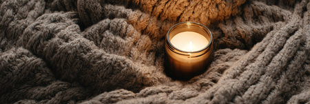 Soft candlelight flickers gently beside a textured, knitted blanket, creating a warm and inviting atmosphere during a cool evening.の素材