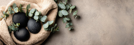 Smooth black stones are surrounded by eucalyptus leaves on a beige towel, creating a calming atmosphere for spa and wellness.の素材