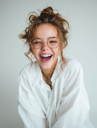 A young woman with curly hair and transparent glasses is laughing joyfully.の素材