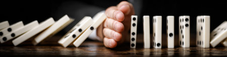 A man stops a line of falling dominoes with his hand, representing control and problem-solving in a simple yet powerful composition.の素材