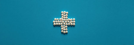 A creative arrangement of white pills forms a medical cross on a bright solid background, serving as an ideal space for advertisements.の素材