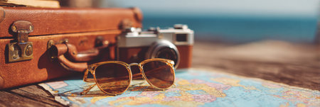Sunglasses and a vintage camera rest on a wooden table near a beach, suggesting a joyful travel experience in sunny weather.の素材