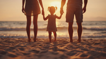 Parents hold their small childrens hands as they walk along the sandy beach during a calm sunset, surrounded by gentle waves.の素材