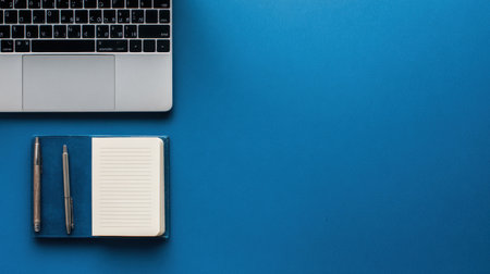 A laptop, notebook, and pen are neatly arranged on a blue background, ideal for study or work activities during the day.の素材