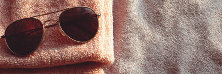 Sunglasses lay casually on a soft folded towel, capturing the essence of summer relaxation by the beach.の素材