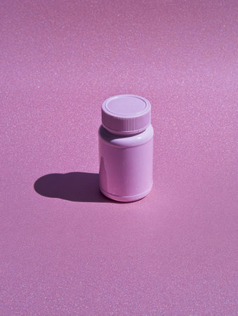 A pill bottle stands on a pastel pink surface, casting a delicate shadow. The light creates a soft and calming atmosphere in this scene.の素材