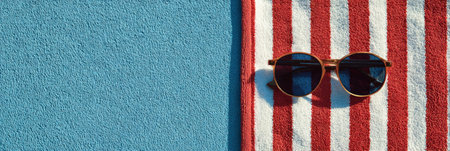 Sunglasses sit on a red and white striped towel next to a clear blue pool, perfect for a relaxing summer afternoon.の素材