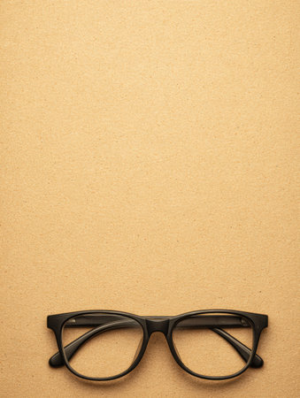 Black frame glasses are positioned on a beige paper background, providing a clean and simple layout for design purposes.の素材