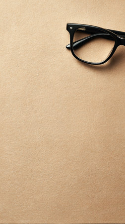 Black frame glasses rest on a smooth beige paper surface, creating a clean and minimalistic style with plenty of space for ideas.の素材