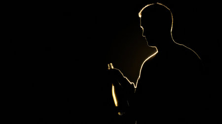 Silhouette of a winemaker holding a bottle, illuminated by soft gold light, creating a striking contrast against a dark backdrop.の素材