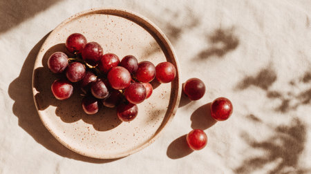 Grapes are neatly arranged on a ceramic plate, showing their natural imperfections under soft afternoon light and gentle shadows.の素材