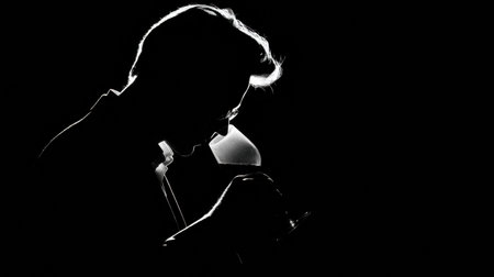 A sommelier takes a moment to savor the aroma of wine from a glass, illuminated by a spotlight in a dimly lit room.の素材