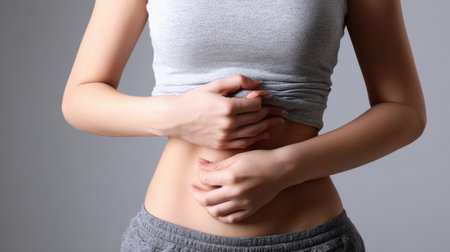 Woman performs a front view belly pressure test, pressing her stomach inward to examine shape and fat fold in a medical aesthetic context.の素材