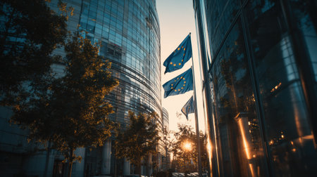 Flags of the European Union fly against a stunning sunset backdrop, casting warm light on modern city architecture and trees.の素材