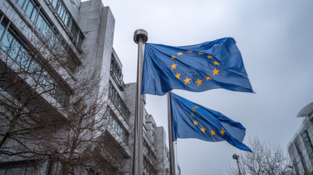 Flags representing the European Union are displayed prominently outside the EU Commission building in Brussels on a gray day.の素材
