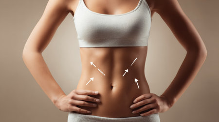 Abdomen close-up showing targeted fat reduction areas with arrows on a clean beige background, featuring studio lighting for clarity.の素材