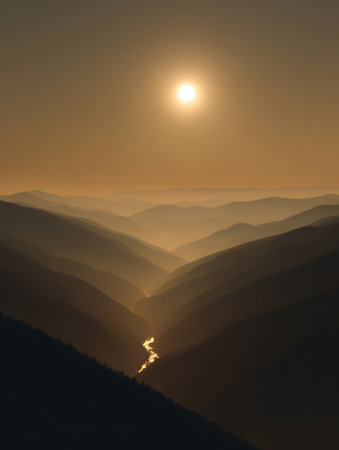 Sunrise lights up a mountain valley, showing mist over ridges and the glow reflecting on a river below during early morning hours.の素材