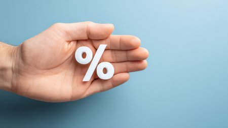 A human hand is holding a percent symbol on a blue background, illustrating themes related to finance and business discussions.の素材
