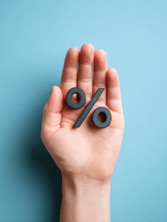 A hand is seen holding a percent symbol against a blank blue background. This scene relates to financial topics such as mortgages or taxes.の素材