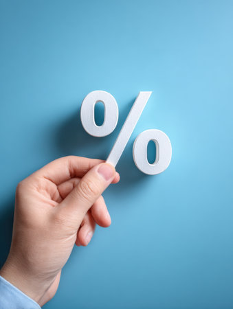 A hand is holding a percent symbol against a blue background to illustrate ideas in finance, business dealings, and pricing strategies.の素材