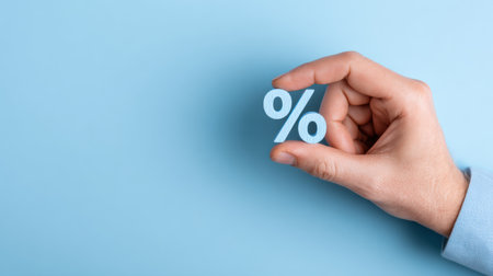 A hand holds a percent symbol against a blue background, illustrating themes of finance, business, and discount strategies in a simple manner.の素材