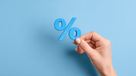 A hand holds a percent symbol on a blue background, representing business, finance, rates, discounts, and tax concepts relevant to clients.の素材