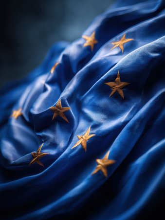 The European Union flag features a deep blue fabric with golden stars arranged in a circle, symbolizing unity among nations, lit artistically.の素材