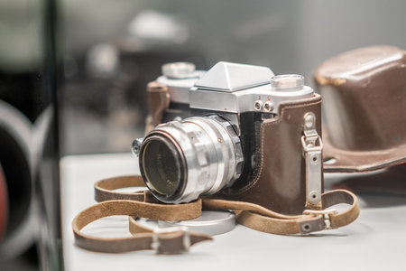 A vintage camera sits in a glass display at a museum, featuring a leather case and strap,...