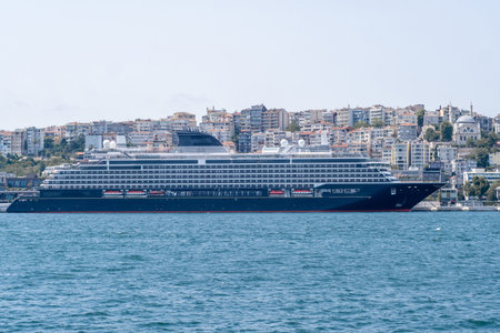 A grand cruise ship sails quietly along the Bosphorus, framed by a lively cityscape under clear blue skies and bright sunlight, reflecting a vibrant atmosphere.の写真素材