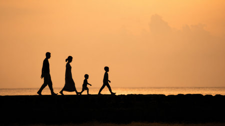 Family walks along the shore at sunrise enjoying time together in the warm light with space above for text and messages for newsletters or adsの素材
