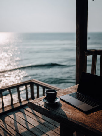 A balcony desk holds a laptop and coffee, offering a view of the ocean horizon during the early morning hours.の素材