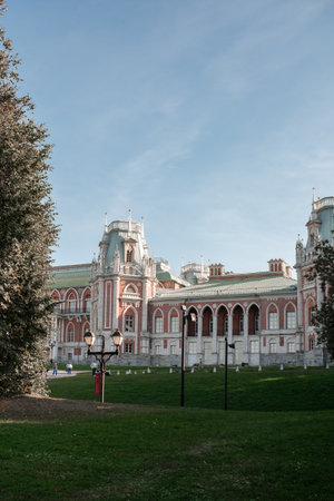 Visitors stroll through the serene park of Tsaritsyno, admiring the grand architecture of the palace under a clear blue sky in a tranquil afternoon setting.の写真素材