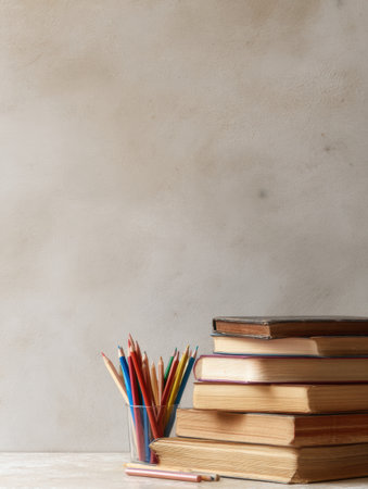 Books are stacked next to a cup filled with colored pencils on a neutral background in a simple environment focused on education.の素材